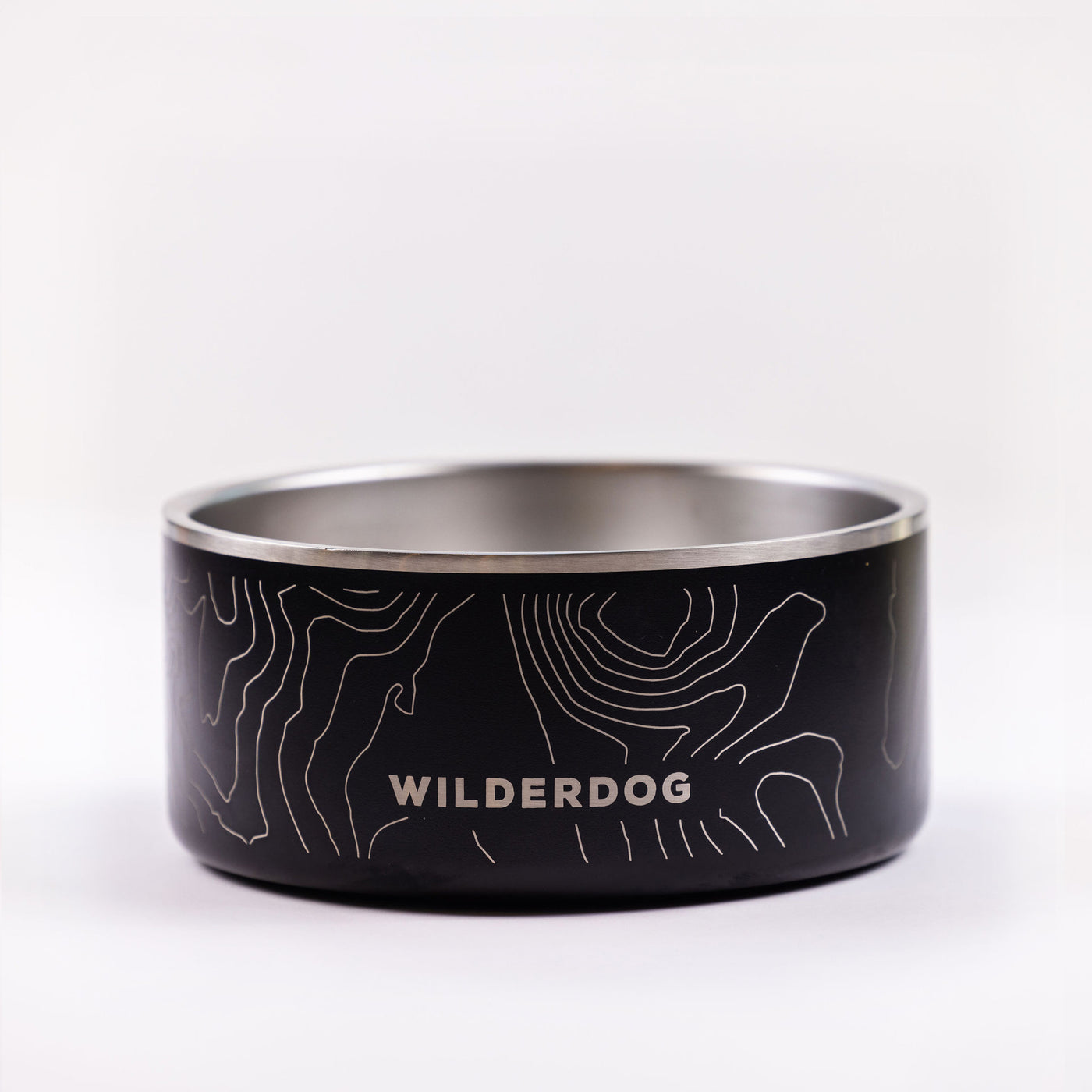 A Stainless Steel Dog Bowl in black with "WILDERDOG" written on the side in white uppercase letters. The BPA-free bowl boasts a white topographic map design etched around its exterior and is showcased against a plain white background.