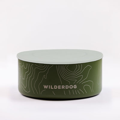 A round green Stainless Steel Dog Bowl with a light green lid, adorned with white line art of topographic maps and the word "WILDERDOG" printed in white on the side. This BPA-free dog bowl is set against a plain white background.