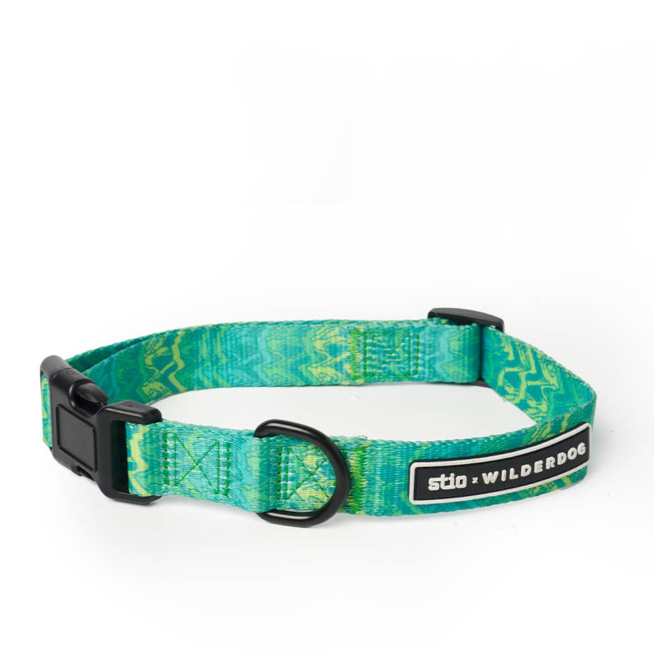 Introducing the Wilderdog x Stio Ultralight Collar: a vibrant green and turquoise dog collar crafted from durable, lightweight nylon webbing with striking zigzag patterns. It features a sturdy black plastic buckle, a metal D-ring for easy leash attachment, and a sleek black tag with "sto x WILDERDOG" branding.