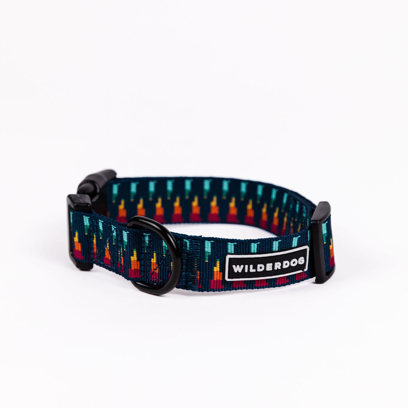 The Marina Ultralight Collar from the Ultralight Collection features a geometric pattern with multicolored vertical lines. Made with ultralight nylon webbing, it includes a heavy-duty plastic clip, a metal D-ring, and a "WILDERDOG" label in white text on a black background. The collar is displayed on a white background.