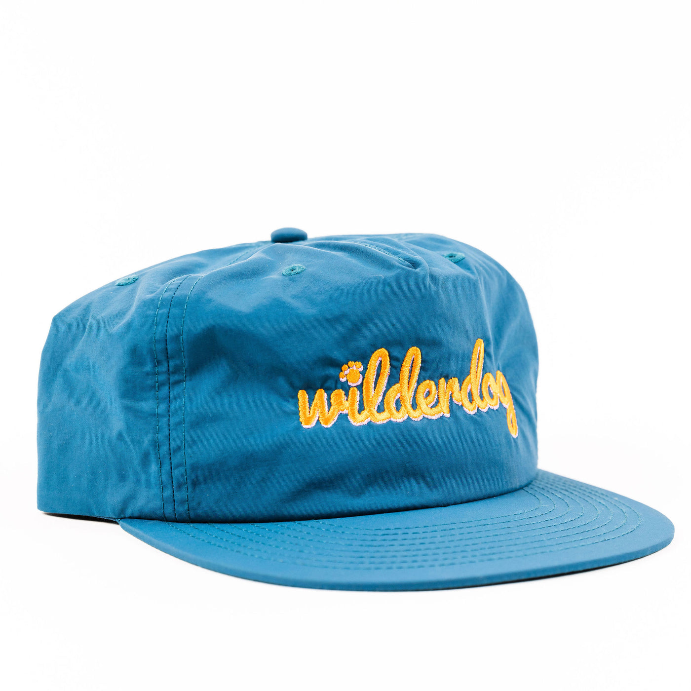 The Wilderdog Surf Hat is a lightweight, quick-dry, blue snapback cap made from recycled nylon, featuring "wilderdog" embroidered in yellow cursive lettering across the front. It is displayed at an angle against a white background, showcasing both the front and part of the side - perfect for any adventure.