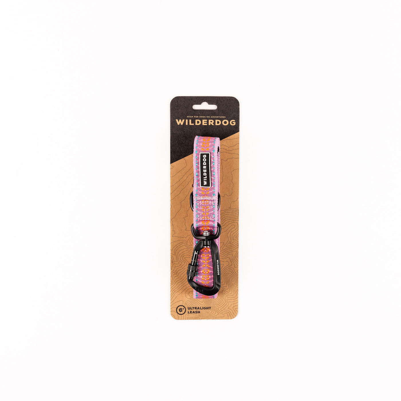 Packaged Wilderdog dog collar in a pink and orange geometric pattern. The collar is rolled and attached to a brown cardboard backing, with text indicating it's from the Wilderdog Ultralight Collection and includes a "Lilac Ultralight Leash." A metal D-ring, buckle, and padded handle are visible.