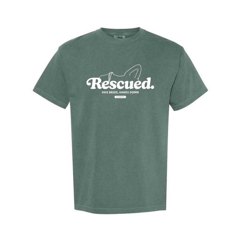 The Wilderdog Rescue Tee is an eco-friendly green Garment-Dyed Heavyweight T-Shirt that showcases a white graphic of dog ears along with the phrase "Rescued. Fave breed, hands down." It's ideal for individuals who want to express their passion while supporting environmental sustainability.