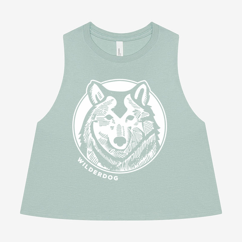 Introducing the Wilderdog Wolf Cropped Racerback Tank: a light green, sustainably produced sleeveless crop top adorned with a white stylized graphic of a wolf's head encircled by a ring. The word "WILDERDOG" is prominently displayed beneath the wolf graphic, all set against a plain white background.